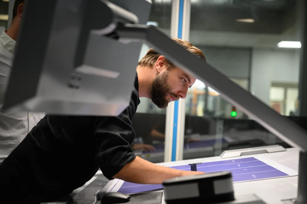Ein Mitarbeiter prüft am Drucktisch konzentriert die Einstellungen der Druckfarben. 