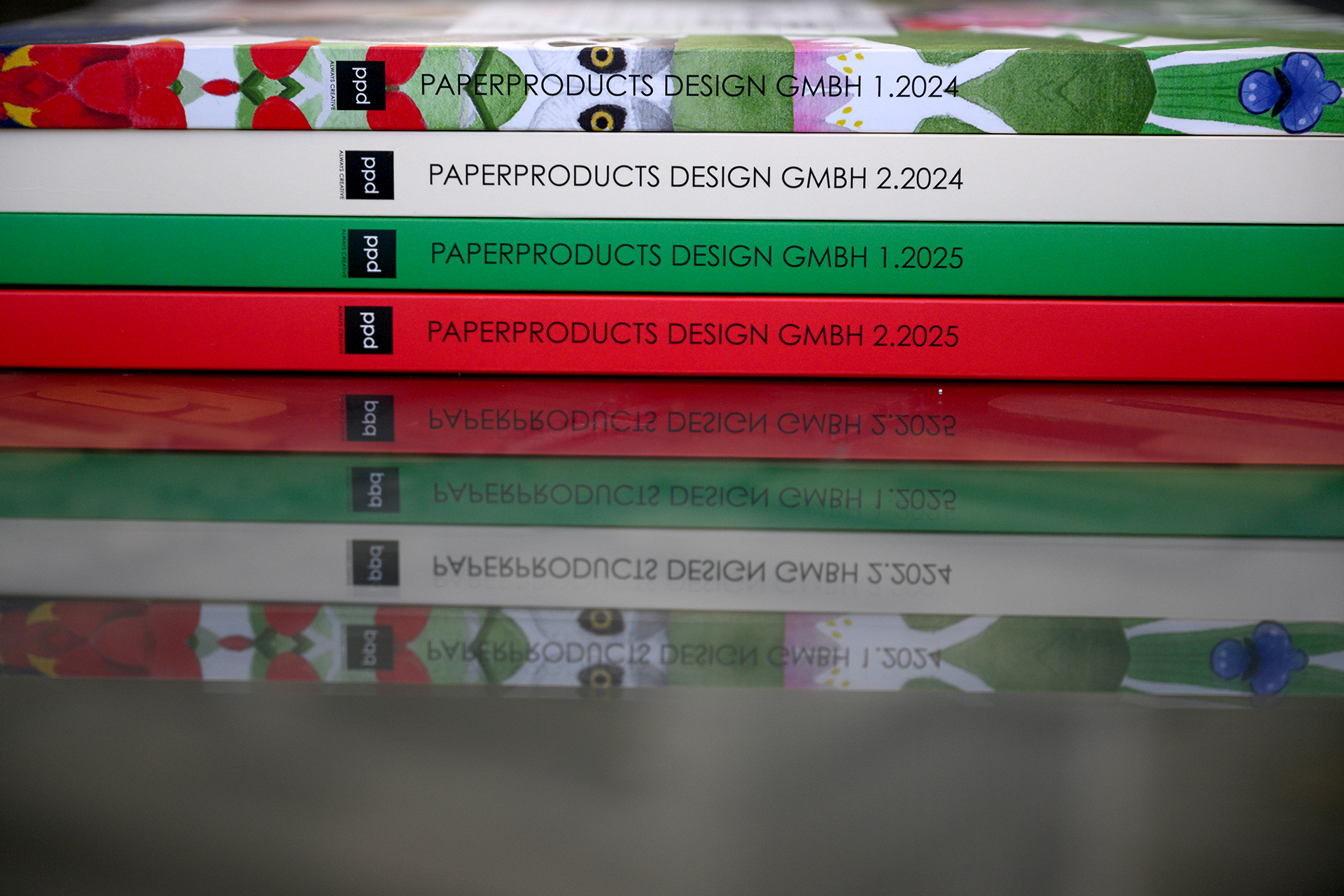 2025_Warlich_Druck_Meckenheim_August_JR_01881 Vier verschiedenartige Bücher, auf deren Rücken PaperproductDesign steht, liegen übereinander